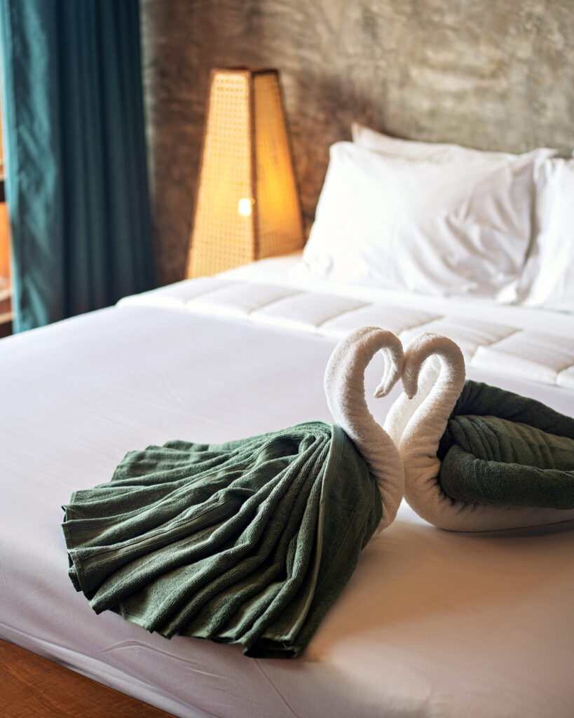 Towel swans on a freshly made bed beside a woven lamp