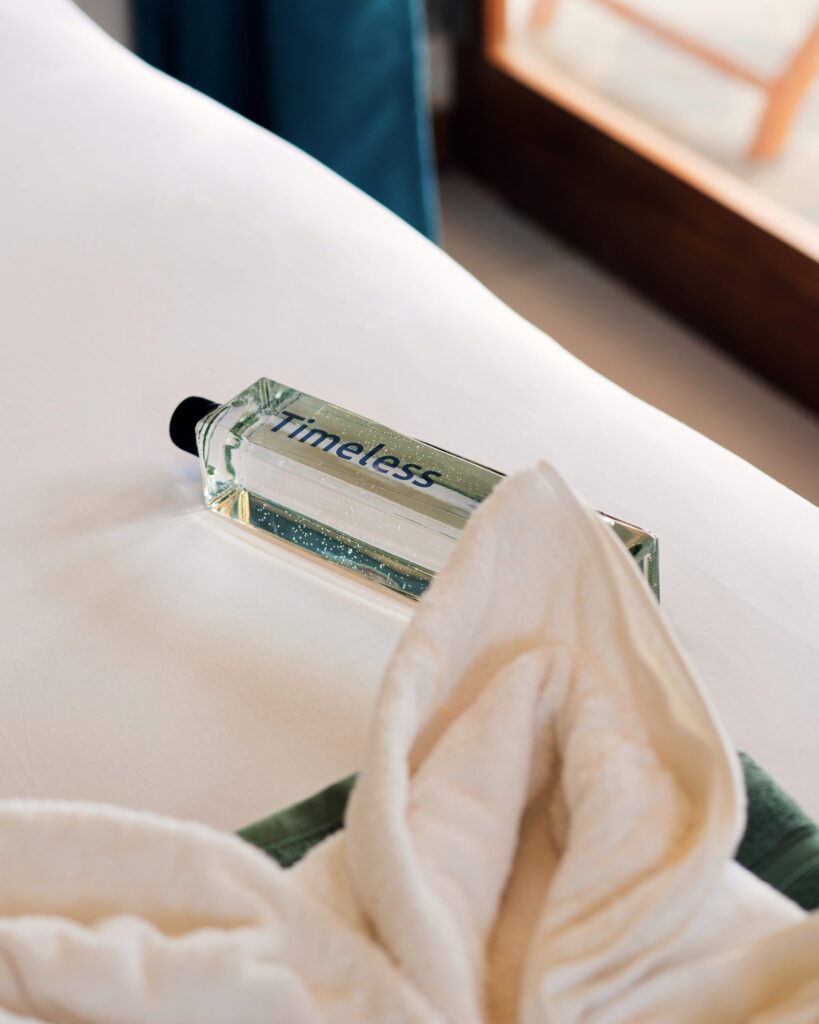 A Timeless bottle and a folded towel resting on a white pillow