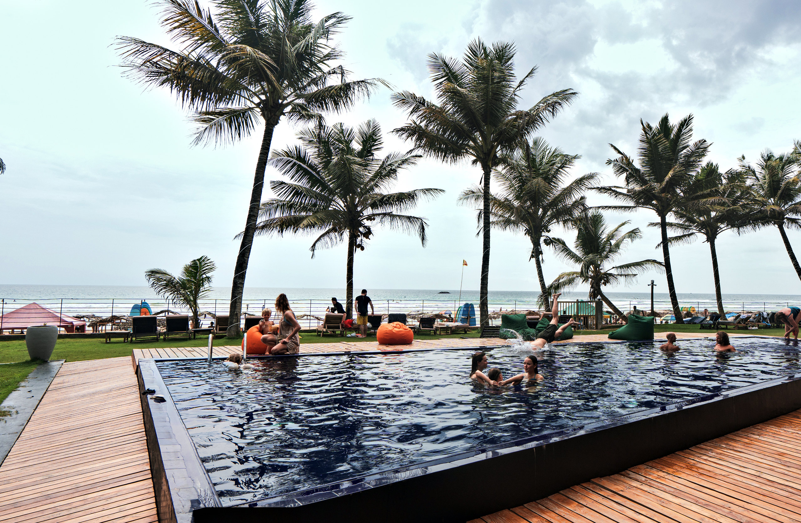 The pool and timber deck at Timeless Beach Hotel, with the palm line and the sea behind