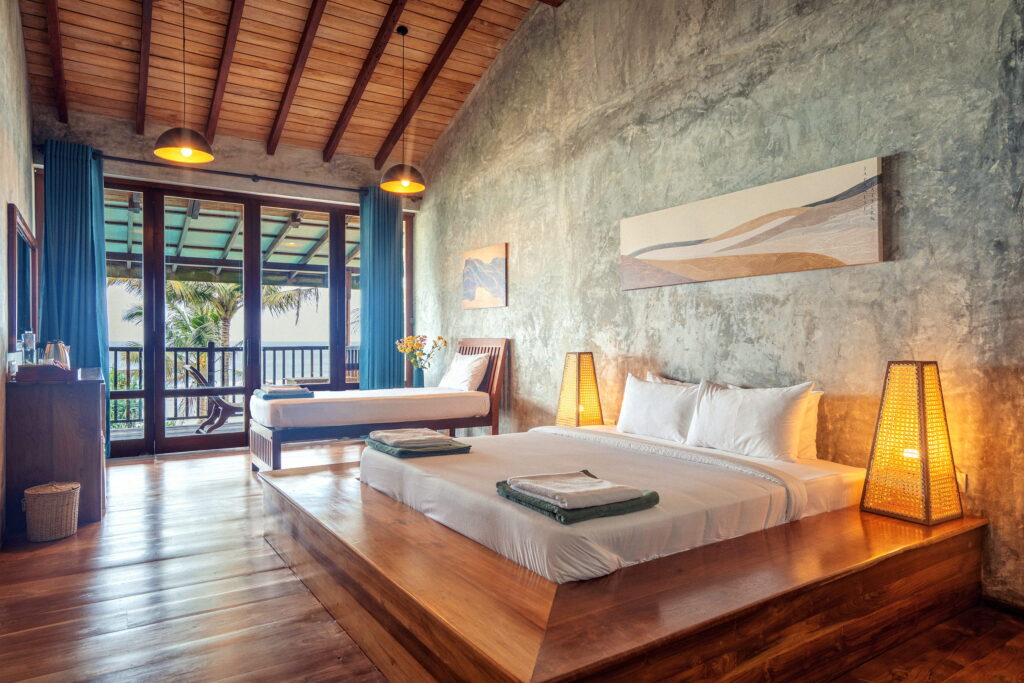 Guest room with a polished concrete wall, a bed on a teak platform and woven lamps