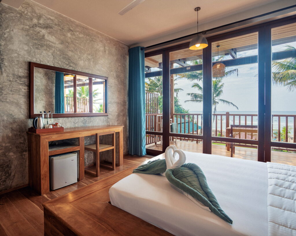 Guest room with a polished concrete wall, a teak desk and towels folded on the bed