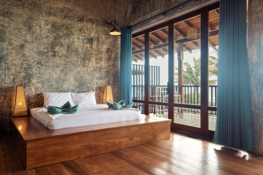 Bed on a teak platform beside glass doors that open to the palms