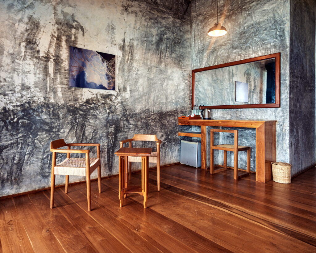 Teak writing desk, mirror and chairs against a textured concrete wall