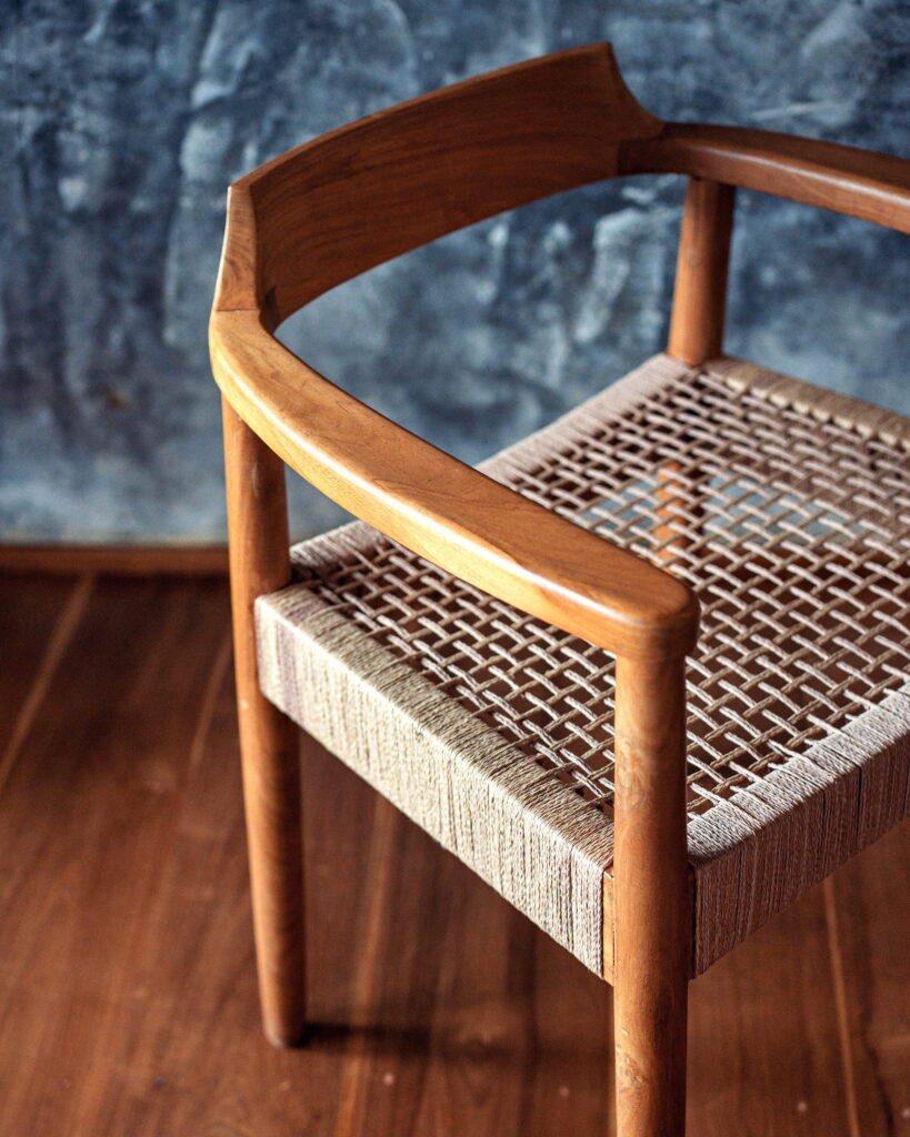 Teak chair with a woven seat against a concrete wall